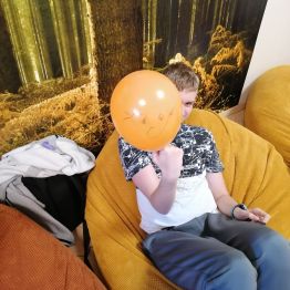 Uczeń leży na pufie i pokazuje pomarańczowy balon