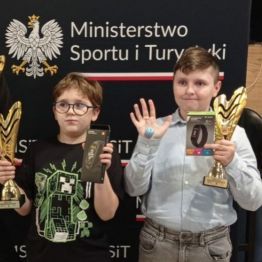 Zadowoleni wychowankowie odbierają puchary w klubie bilardowym.