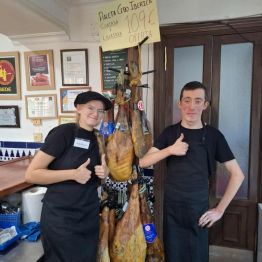 Uczniowie stoją przy wieszaku z suszonymi szynkami 