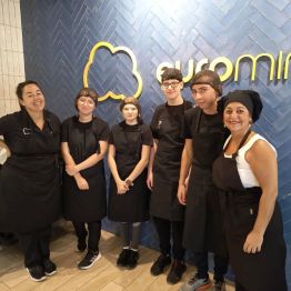 Uczniowie w czarnych fartuchach i czepkach z dwiema paniami podczas praktyk