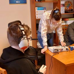 Siedzący chłopiec w trakcie badania słuchu, obok protetyk.