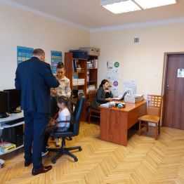 Trzy osoby dorosłe - protetycy słuchu omawiają wynik badania siedzącej na fotelu dziewczynki.