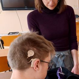 Mężczyzna z widocznym implantem słuchowym, obok prowadząca szkolenie. 