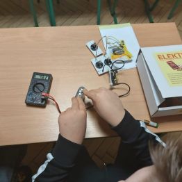 Wychowanek dokonuje pomiaru napięcia baterii przy użyciu prostego miernika cyfrowego.