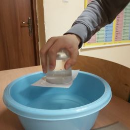 Wychowanek wykonuje doświadczenie "zaczarowana szklanka". Mamy miskę, szklankę wypełniona wodą do pełna, na szklankę kładziemy kawałek papieru z bloku technicznego lub rysunkowego. Przytykamy papier ręka do szklanki i odwracamy do góry dnem. Woda ze szklanki nie wylewa się. Obserwujemy zjawisko i odpowiadamy dlaczego woda ze szklanki nie wylewa się? Bo działa ciśnienie atmosferyczne!