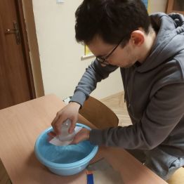 Wychowanek wykonuje doświadczenie "zaczarowana szklanka". Mamy miskę, szklankę wypełniona wodą do pełna, na szklankę kładziemy kawałek papieru z bloku technicznego lub rysunkowego. Przytykamy papier ręka do szklanki i odwracamy do góry dnem. Woda ze szklanki nie wylewa się. Obserwujemy zjawisko i odpowiadamy dlaczego woda ze szklanki nie wylewa się? Bo działa ciśnienie atmosferyczne!