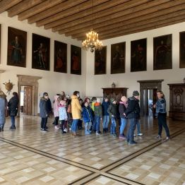 Grupa uczniów stoi we wnętrzu Pałacu, wysłuchując informację od przewodnika.