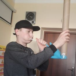 chłopiec używa instrumentu muzycznego zrobionego przez siebie z tuby, rękawiczki i słomki
