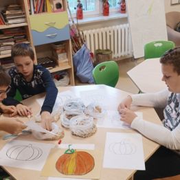 Chłopcy wykonują dyniową pracę plastyczną z jej własnych pestek i kolorowych ziaren.