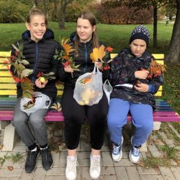 Ola, Krzyś i Wojtek siedzą na ławeczce w parku. W rękach trzymają dary jesieni.