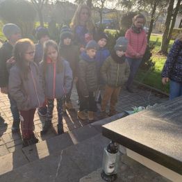 Uczniowie klas I stoją w zadumie przy pomniku upamiętniającym ofiary okupacji.