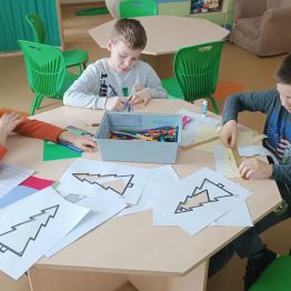 Chłopcy przygotowują choinki z kolorowych pasków papieru.