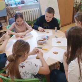 Grupa uczniów dekoruje świąteczne pierniczki.
