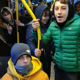 Jeden chłopiec stoi a drugi siedzi w autobusie. 