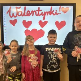 Uczniowie klasy 1 c, stoją przed tablicą walentynkową ze swoimi upominkami.