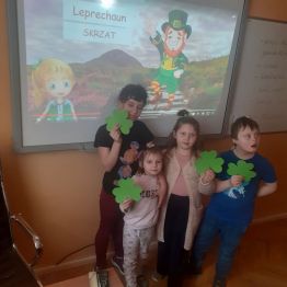 Trzy dziewczynki i chłopiec trzymają w rękach papierowe koniczyny.