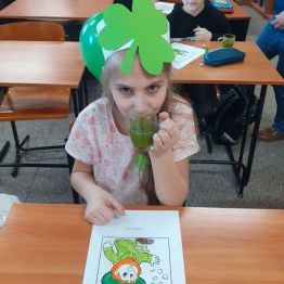 Dziewczynka w opasce z zieloną koniczyną zrobioną z papieru pije zielony koktajl