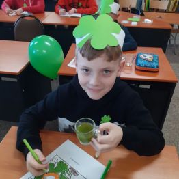 Chłopiec w jednej ręce szklankę z zielonym koktajlem, a w drugiej zieloną kredkę. Na ławce leży kolorowanka św. Patryk.