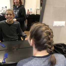 Krzyś siedzi na fotelu i przegląda się w lustrze. Ma piękny warkocz francuski. Z tyłu stoi Ola z kl. 3 b BS.