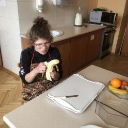 Hania siedzi przy stole i obiera banana.
