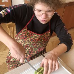 Hania siedzi przy stole i kroi kiwi.