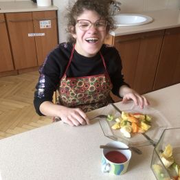 Hania siedzi przy stole i się uśmiecha. Na stole leży talerz z gotowym, kolorowym i zdrowym deserem owocowym.