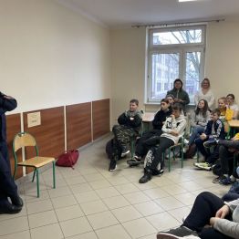 Policjant stoi przed uczniami siedzącymi w szkolnej stołówce.