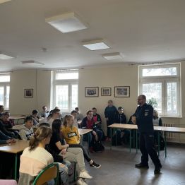 Grupa uczniów w szkolnej stołówce słucha przemawiającego policjanta