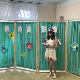 Uczennica z wiankiem na głowie. Za nią parawan z wiosennymi dekoracjami.