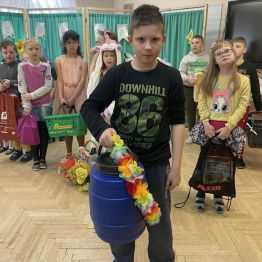 Chłopiec trzymający w ręku niebieską beczkę. Za nim inne dzieci.