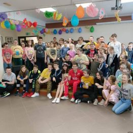 Duża grupa uczniów siedzi na scenie. Wśród nich sportowiec - Maksym Chudzicki.