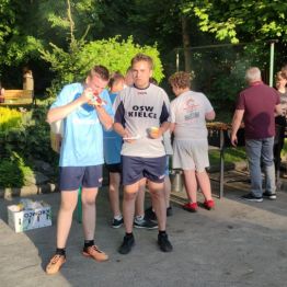 Chłopcy jedzą kiełbaskę przy grillu.