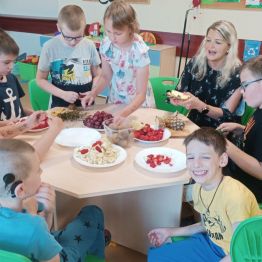 Grupa wychowanków z wychowawczynią obierają owoce ze skóry i kroją w plasterki..
