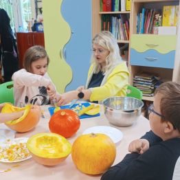 Grupa uczniów wraz z wychowawczynią kroją miąższ dyni w kostkę i oddzielają pestki od dyni.