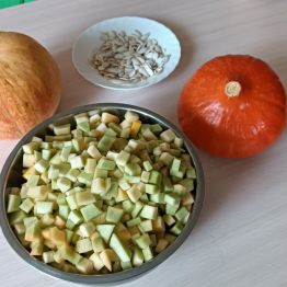 Pokrojona dynia w kostkę w misce. Dynie w całości. Wydrążone pestki dyni.