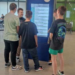 Pięciu chłopców zapoznaje się z tablicą informacyjną na dworcu PKS.