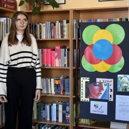 Uczennica podczas recytacji wiersza w bibliotece szkolnej. W tle regał z książkami. 