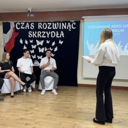 Uczennica na środku sceny zwraca się do absolwentów.