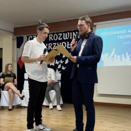 Uczeń w garniturze przeprowadza wywiad z absolwentem.
