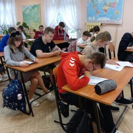 Uczniowie siedż przy stolikach i piszą test z historii