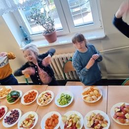 Dzieci stoją przy stole, na którym leżą pokrojone owoce na talerzykach