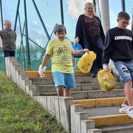 Wychowankowie wokół boiska zbierają śmieci.