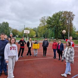 Wychowankowie stoją w kole, przygotowują się do rozgrzewki. Chłopiec trzyma piłkę w ręce.