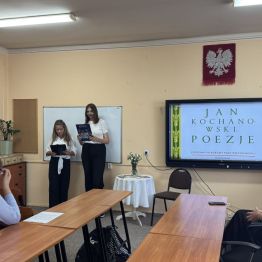 Uczestnicy Narodowego Czytania patrzą w stronę tablicy multimedialnej i uczennic prowadzących wydarzenie