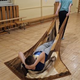 Wychowanek ciągnie kocyk z kolegą, który leży na plecach.