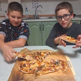 Chłopcy konsumują swoją pizzę.