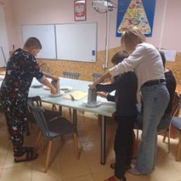 Wychowawca pomaga w przygotowaniu pizzy młodszym wychowankom.