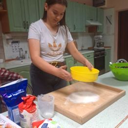 Dziewczynka przesiewa mąkę na placek.