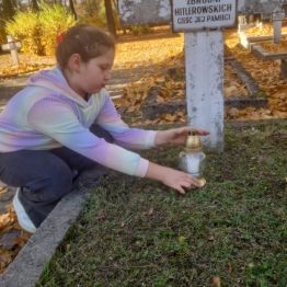 Uczennica zapala znicz na grobie żołnierza