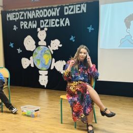 Aktorzy szkolnego teatrzyku podczas przedstawienia - uczennica rozmawia przez telefon, młodszy uczeń wyciąga coś z plecaka.